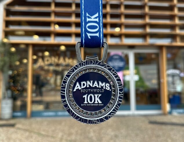 Adnams 10k Run 2025 medal hanging ready outside of the Adnams Southwold store, an upcoming event in Southwold.